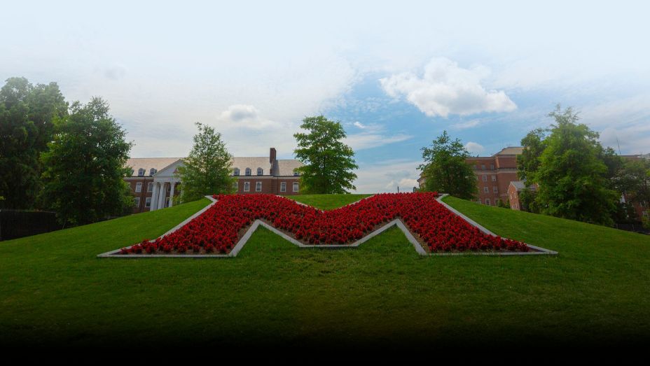 large "M" in flowers on a lawn in front of a traditional building